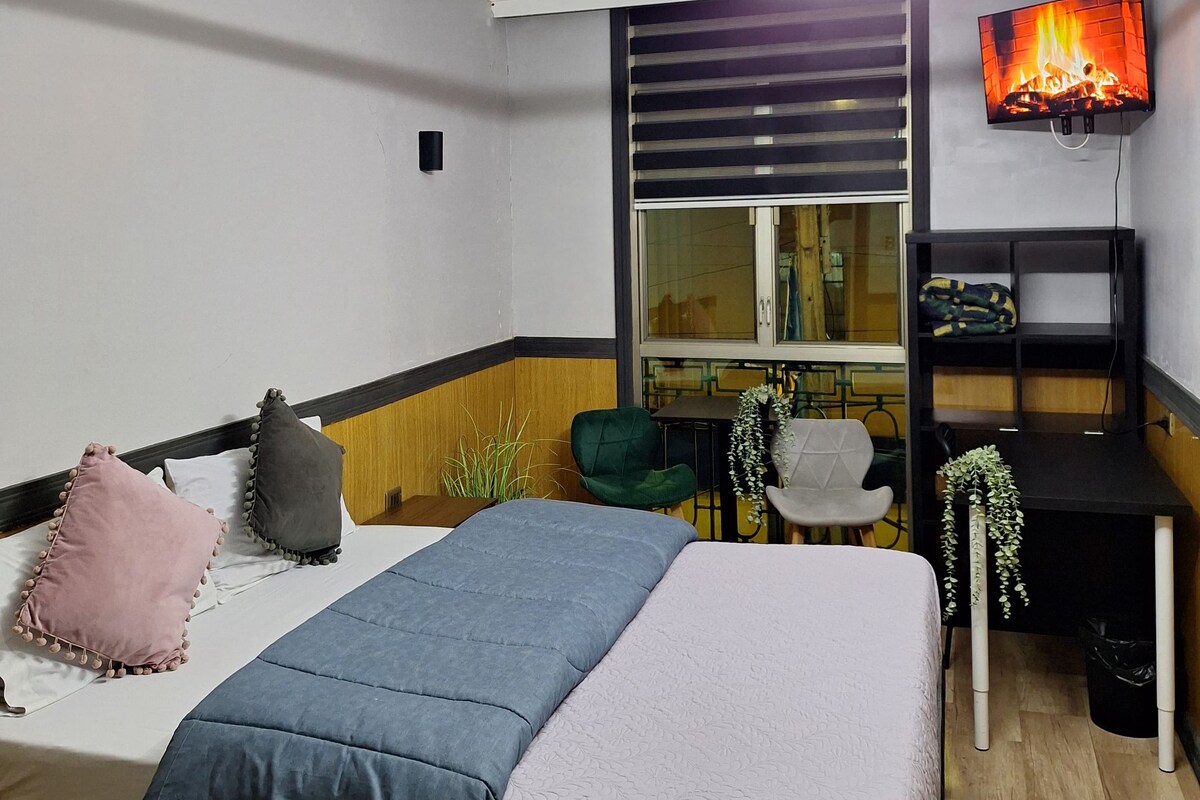 A modern bedroom with a bed, bedside tables, a TV, and a window.