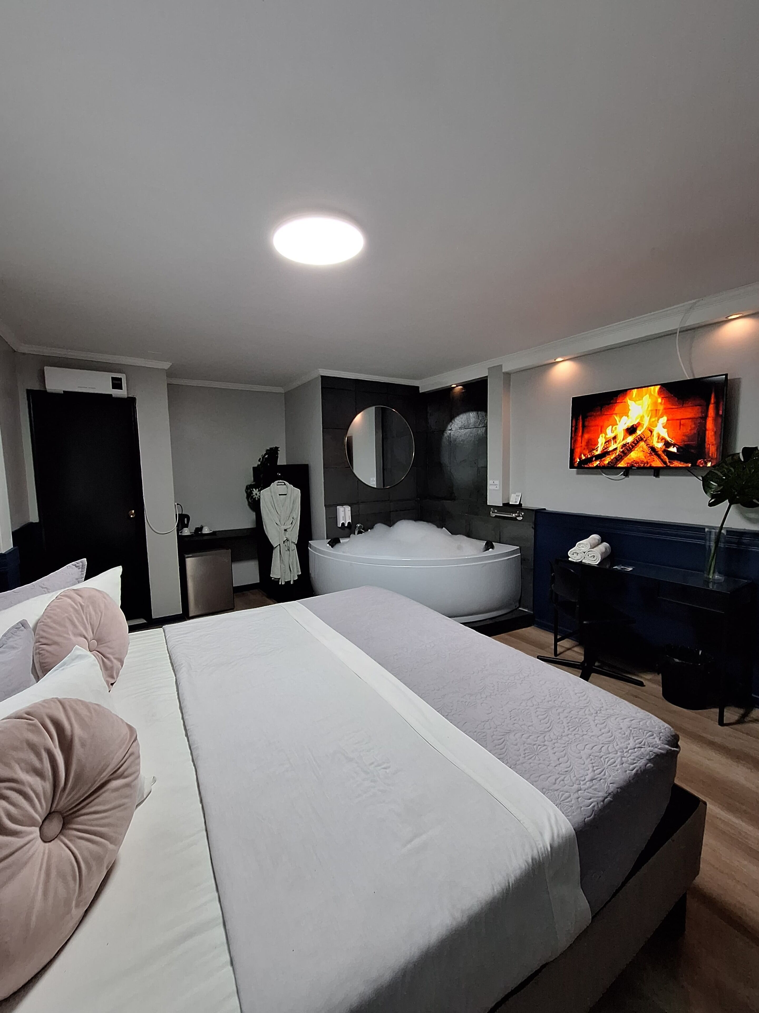 A modern hotel room with a large bed, a bathtub, a TV, and a desk.