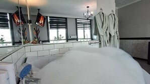 A modern bathroom with a large bathtub filled with bubbles, a shower area, and a vanity with a mirror. - Hotel Asturias (Vina del Mar)