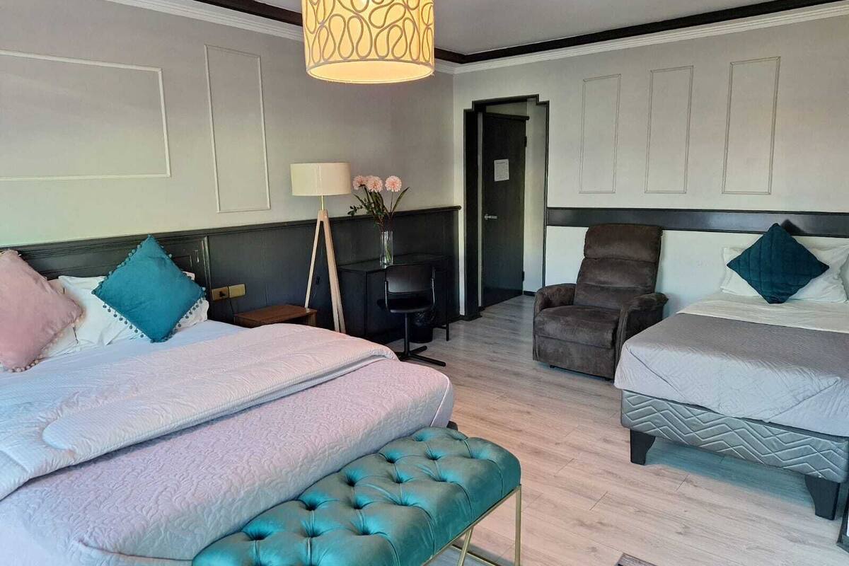 A hotel room with two beds, a desk, a chair, and a hanging light fixture.