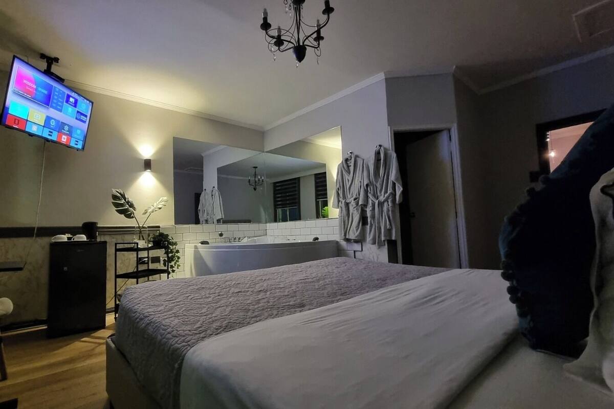 A hotel room with a bed, a desk, a chair, a TV, a mirror, and a bathroom with a bathtub.