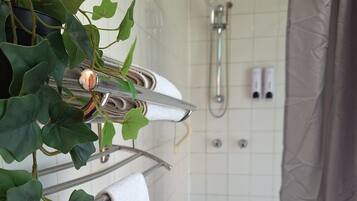 Une salle de bain avec une baignoire, une douche et un porte-serviettes agrémenté d’une plante.