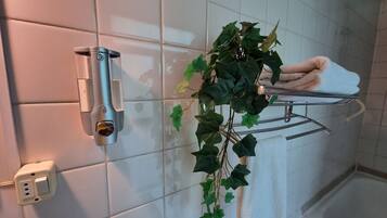 A bathroom with a towel rack, a wall-mounted outlet, and a potted plant.