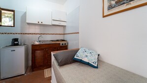Una cocina compacta con armarios blancos, un refrigerador pequeño y una estufa. Hay una cama con un cojín estampado y una alfombra en el suelo.