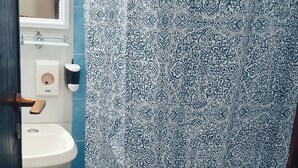 Un baño con lavamanos blanco, inodoro y cortina de ducha con estampado azul y blanco.