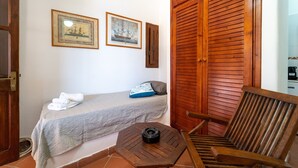 Una habitación con una cama, una mesita, una silla y dos cuadros en la pared.