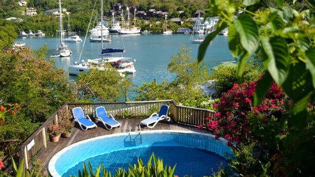 A swimming pool with lounge chairs, surrounded by lush greenery and a view of a marina with boats. - Hibiscus cottage Marigot bay (Marigot bay)