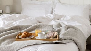 A neatly made bed with white linens, a tray with croissant, orange juice, and a magazine, and a bedside lamp on a nightstand. - Beautiful converted stable near the coast (Plymouth)