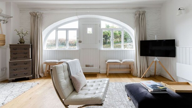A living room with a sofa, a television on a tripod, a wooden bench, and a window with curtains. - Beautiful converted stable near the coast (Plymouth)