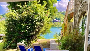 Eine Terrasse im Freien mit Tisch und zwei Stühlen, mit Blick auf ein Gewässer und üppiges Grün.