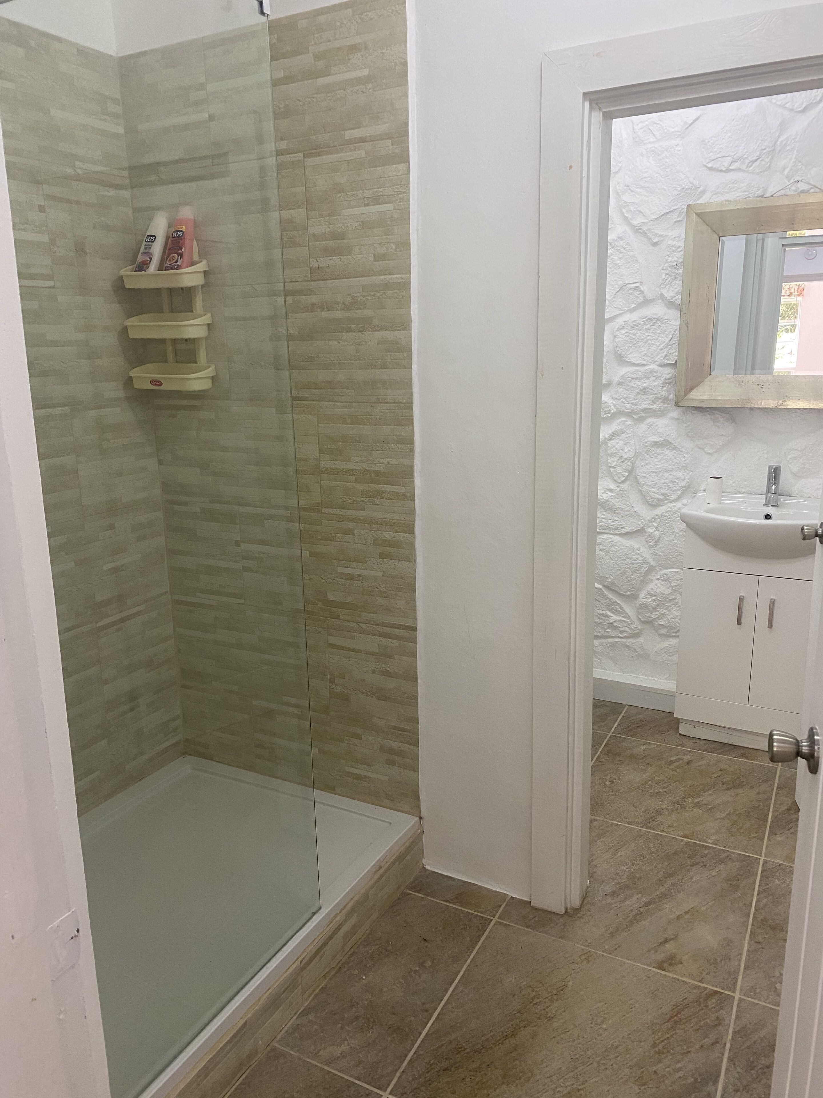 A bathroom with a glass shower enclosure, a white sink with a mirror above it, and a tiled floor.
