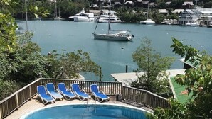 Ein Swimmingpool mit Liegestühlen, umgeben von Grünpflanzen, mit Blick auf einen Yachthafen und Boote.