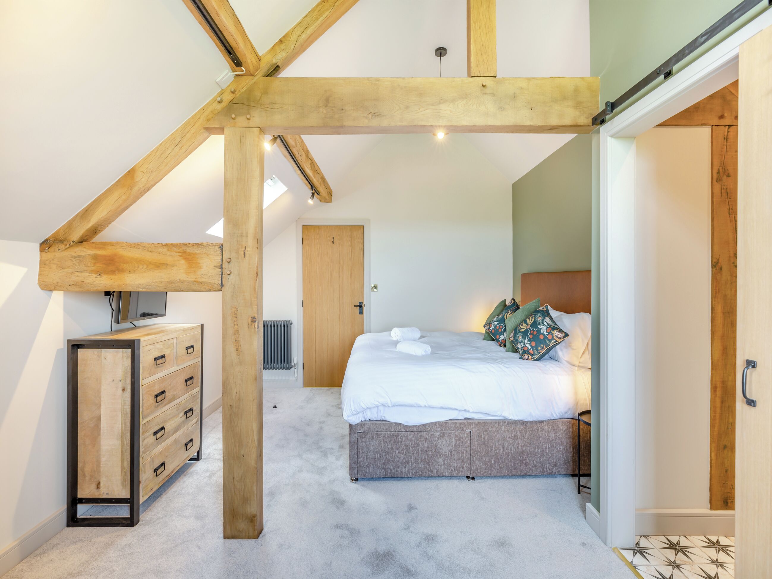 A bedroom with a sloped ceiling, a bed with pillows, a dresser, and a radiator.
