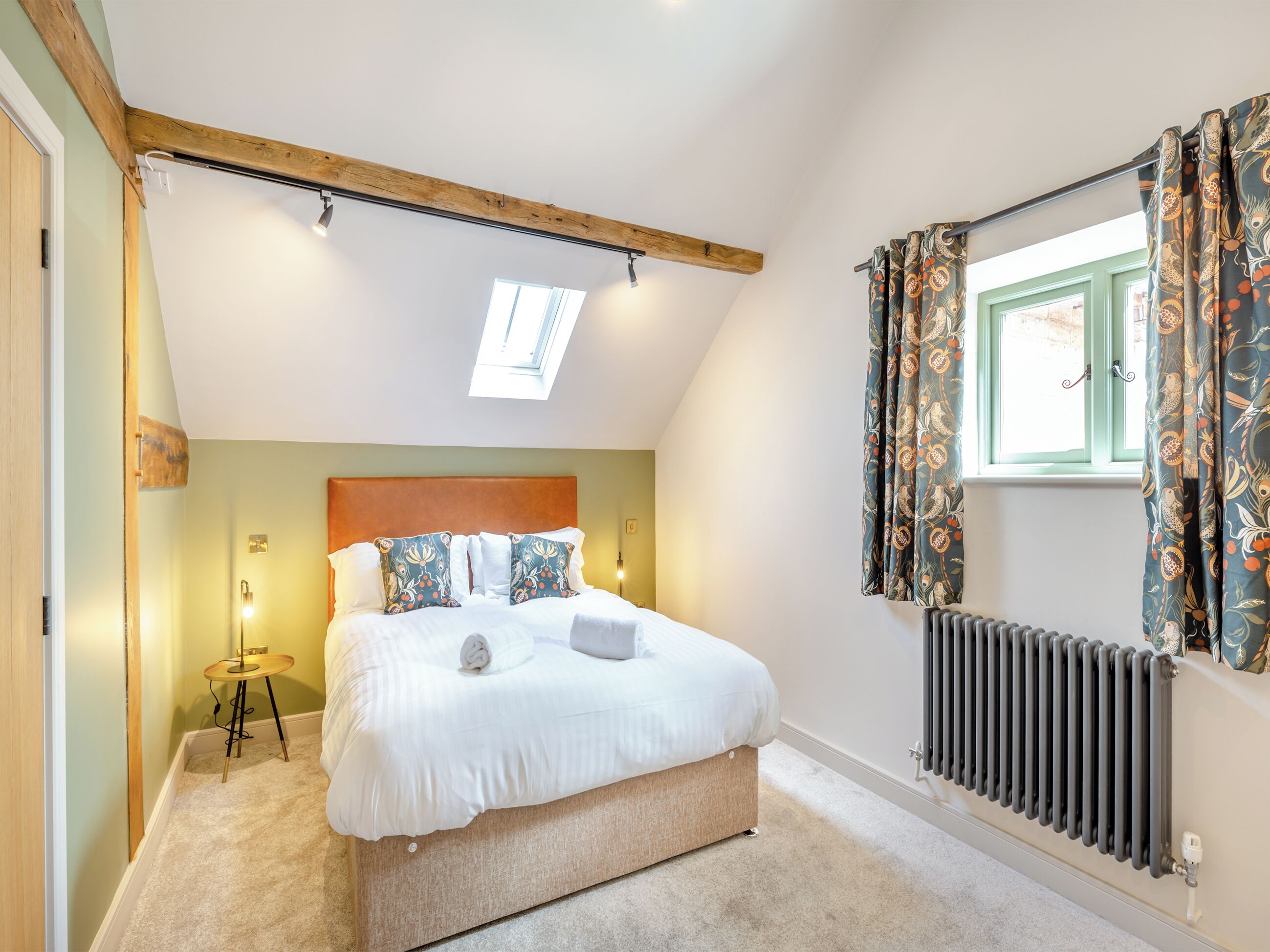 Ein Schlafzimmer mit Bett, Oberlicht, Heizkörper und einem fenster mit Vorhängen.