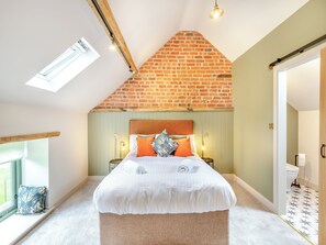 Ein Schlafzimmer mit schrägem Dach, einem Bett, einem Fenster und einer Tür.