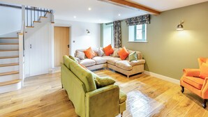 A spacious living area with a wooden staircase, a sectional sofa, a green armchair, and a small orange armchair.