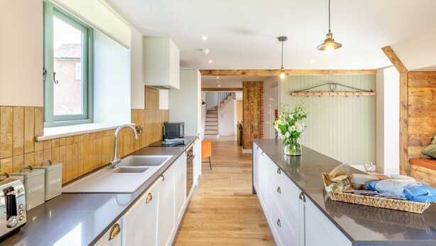 A modern kitchen with a central island, wooden flooring, and a view to a living area.