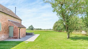 A brick building with a green door, a paved area, and a grassy field with a tree.