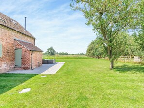 A brick building with a green door, a paved area, and a grassy field with a tree.