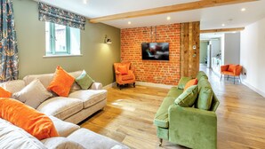 A spacious living area with a brick wall, a flat-screen TV, and a wooden ceiling beam.