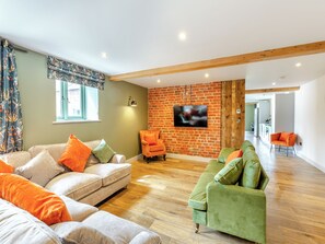 Ein geräumiger Wohnbereich mit Backsteinwand, Flachbildfernseher und Holzbalkendecke.