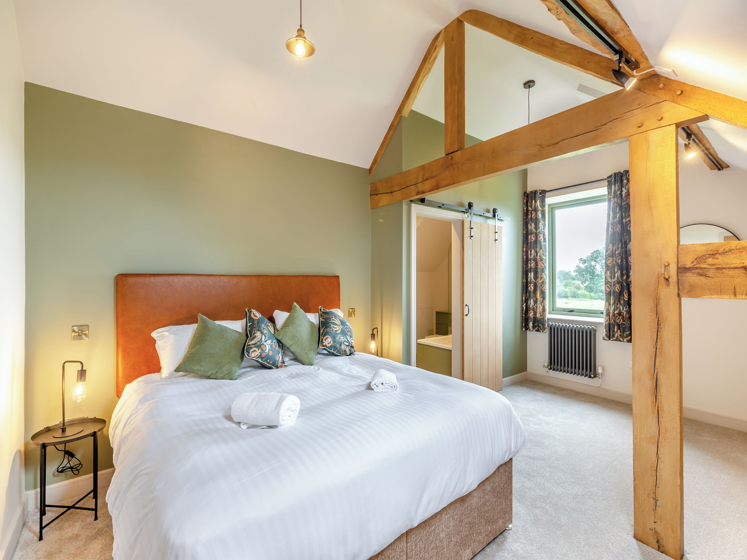 A bedroom with a wooden ceiling, a bed with white linens, and a bedside table with a lamp.