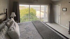 Ein Schlafzimmer mit einem großen Bett, einem Deckenventilator und Blick ins Freie durch eine Schiebetür.