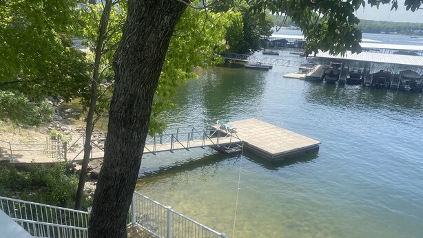 Ein freier Blick auf einen Steg, der sich in ruhiges Wasser erstreckt, umgeben von Bäumen und einem entfernten Gebäude.