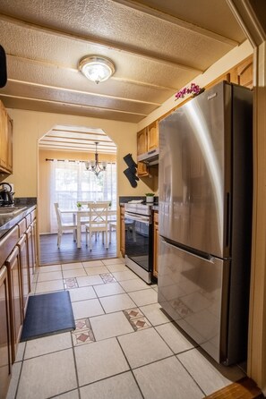 Una cocina con un refrigerador de acero inoxidable, armarios de madera, una mesa de comedor con sillas y un piso de baldosas estampadas.