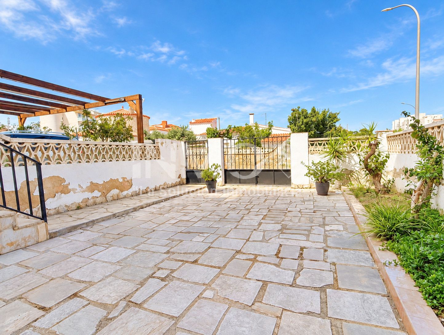 A paved courtyard with stone tiles, a metal gate, and a wooden pergola.