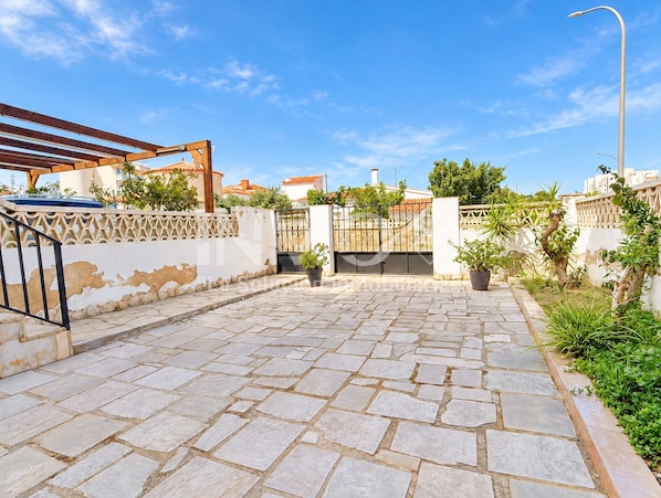 A paved courtyard with stone tiles, a metal gate, and a wooden pergola.