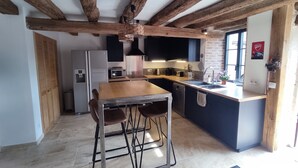 Una cocina con vigas de madera a la vista, una mesa de madera con dos sillas, un horno empotrado y un lavamanos.