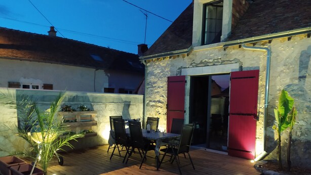 Una terraza de madera con una mesa de comedor y sillas, una planta en maceta y un muro de piedra.