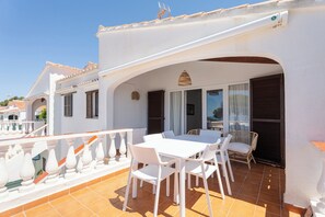 A terrace with a white table and chairs, a wicker chair, and a view of the sea. - V110B | Villa La Pau (Son Bou)