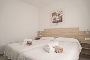 Habitación de hotel con dos camas, cabecera de madera, una obra de arte en la pared y toallas dobladas con cuidado.