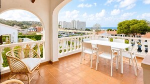 A balcony with white furniture, a wicker hanging light fixture, and a view of buildings and greenery. - V110B | Villa La Pau (Son Bou)