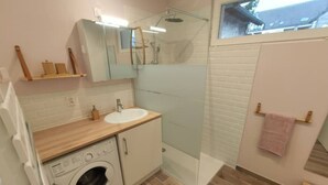 Une salle de bain moderne avec un meuble-lavabo en bois, un lave-linge, une cabine de douche en verre et une petite fenêtre.