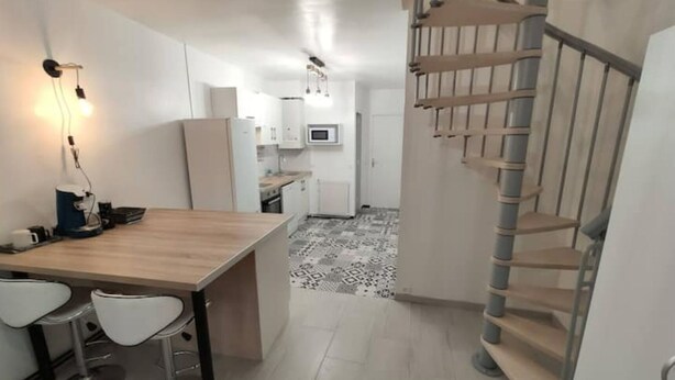 Une cuisine moderne avec un îlot central, des tabourets de bar blancs et un escalier en colimaçon.