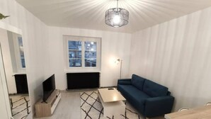 Un salon moderne avec un canapé bleu, un téléviseur, une cheminée et un tapis à motifs.