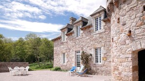 A stone building with a courtyard, outdoor seating, and a large window. - La Grangerie - Charmante demeure typique (Erquy)