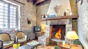 A cozy living room with a stone fireplace, comfortable seating, and a television. - La Grangerie - Charmante demeure typique (Erquy)