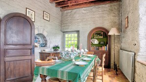 A dining room with a green tablecloth, wooden chairs, and a rustic stone wall. - La Grangerie - Charmante demeure typique (Erquy)