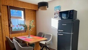 Cocina compacta con una mesa de madera, cuatro sillas, un refrigerador negro y una ventana con vista a una montaña.