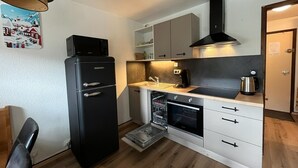 Una cocina compacta con un refrigerador negro, horno integrado, cafetera y lavavajillas.