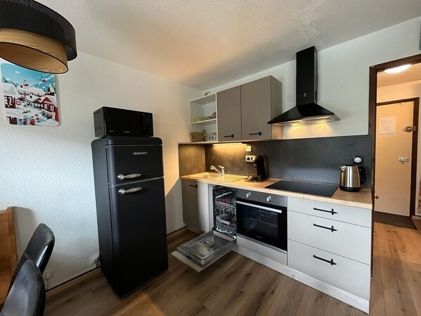 A compact kitchen with a black refrigerator, a built-in oven, a coffee maker, and a dishwasher.