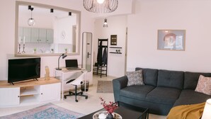 Un salon moderne avec un canapé gris, un téléviseur, un bureau avec un ordinateur portable et un grand miroir.