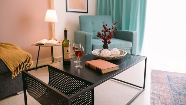 Un salon moderne avec un canapé, une table basse, une lampe, une bouteille de vin, des verres et un livre.
