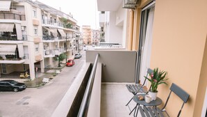 Un balcon avec une table et des chaises, un pot de fleurs et une vue sur une rue animée, avec des voitures et des immeubles.