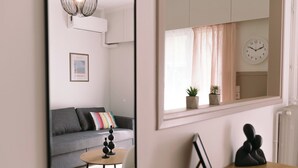 Un salon moderne avec un canapé gris, une petite table ronde, un miroir et une horloge au mur.