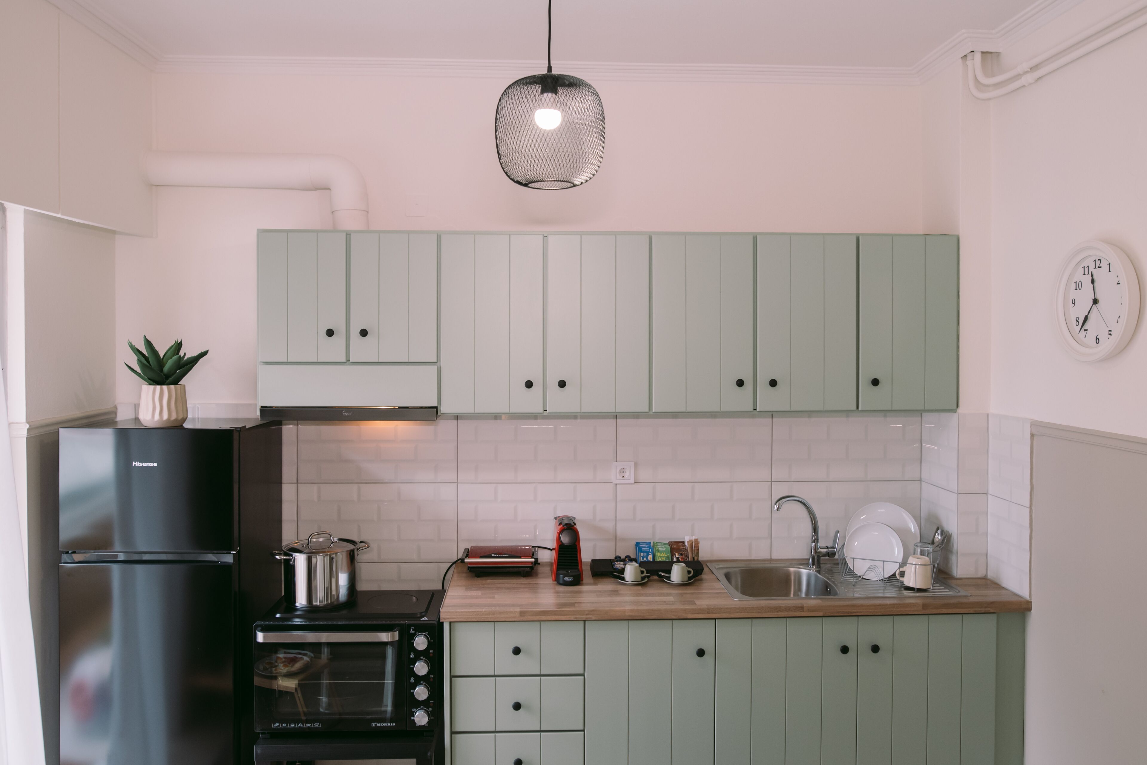 Una cocina con armarios verde claro, un refrigerador negro, una estufa y un lavaplatos.